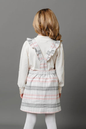 A young girl is seen from behind, wearing a gray and rose plaid overall skirt with ruffle straps.