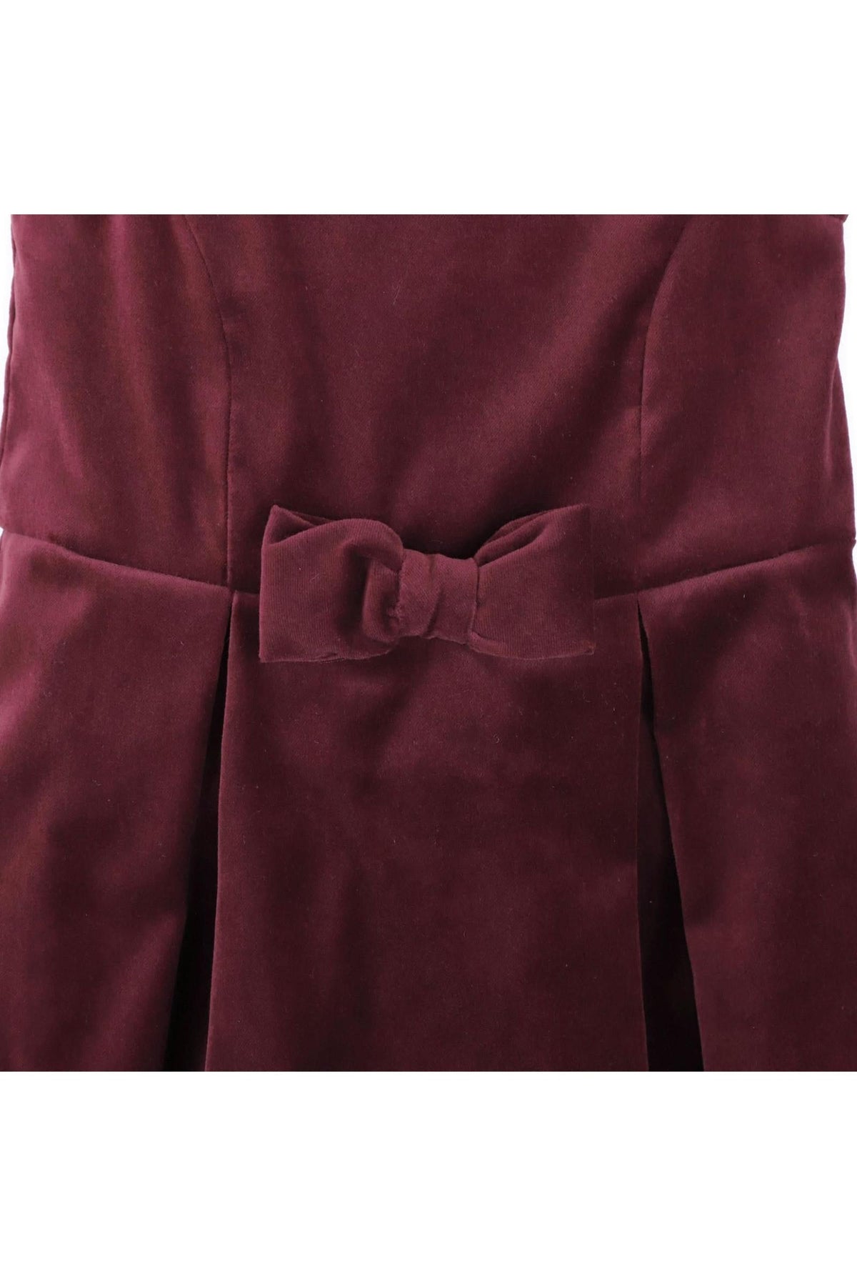 Close-up of a wine red jumper dress featuring a bow front detail and pleated skirt, made from soft organic cotton.