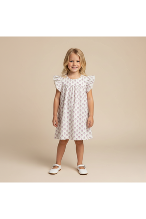 A young girl smiles while wearing a short sleeve, white dress adorned with lavender floral patterns and ruffled sleeves.