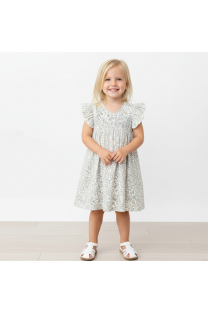 A young girl stands smiling in a floral-patterned dress with flutter sleeves. The dress features a soft, organic fabric, perfect for everyday wear and special occasions.