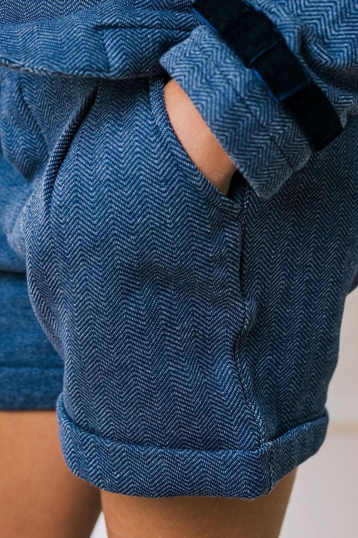 Close-up of blue organic cotton dress shorts featuring a herringbone pattern, cuffed hem, and a side pocket.