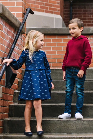 A girl in a navy bicycle print dress stands on stairs, smiling at a boy in a red hoodie and.