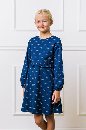 A young girl models a navy dress featuring a bicycle print and a ruffled waist, set against a light background.
