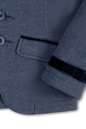 Close-up of a navy blue blazer featuring a herringbone pattern, faux suede piping, and decorative bow at the cuff.