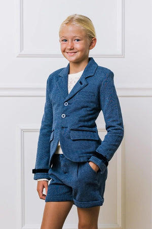 A young girl smiles while wearing a blue herringbone blazer with faux suede accents and matching shorts.