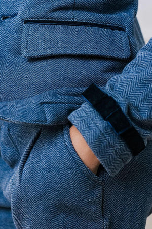 Close-up of a blue herringbone patterned fabric featuring a pocket and a cuff with a black ribbon bow detail.