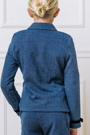 A young girl is seen from the back, wearing a blue herringbone-patterned blazer with long sleeves and a classic collar.