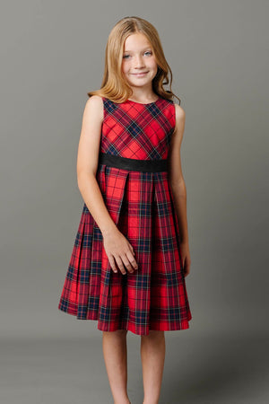 A young girl models a classic red tartan pleated dress with a fitted bodice and a black waistband. The dress features an A-line skirt, perfect for special occasions.