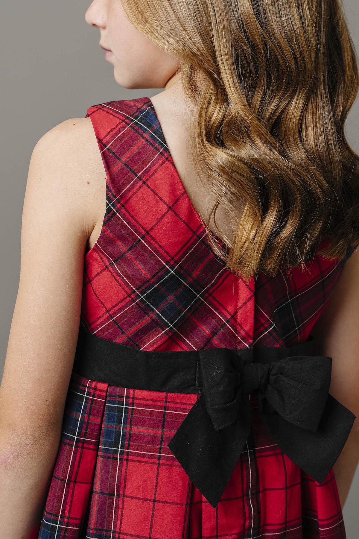 A close-up of a girls red plaid dress featuring a black waist sash with a bow, highlighting the soft fabric.