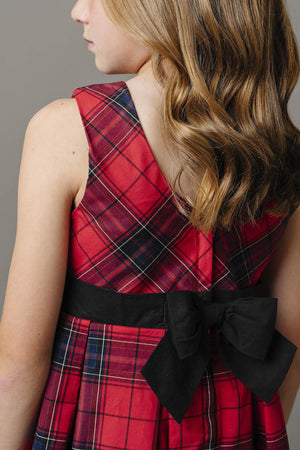 A close-up of a girls red plaid dress featuring a black waist sash with a bow, highlighting the soft fabric.