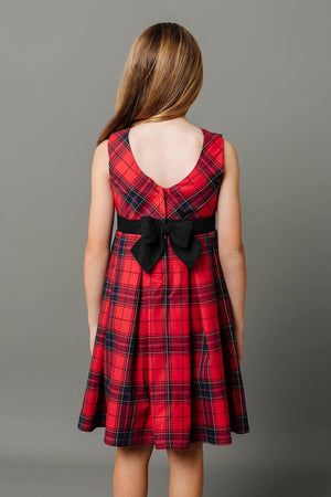 A girl is wearing a red plaid party dress with a black bow at the waist, showcasing a pleated design.