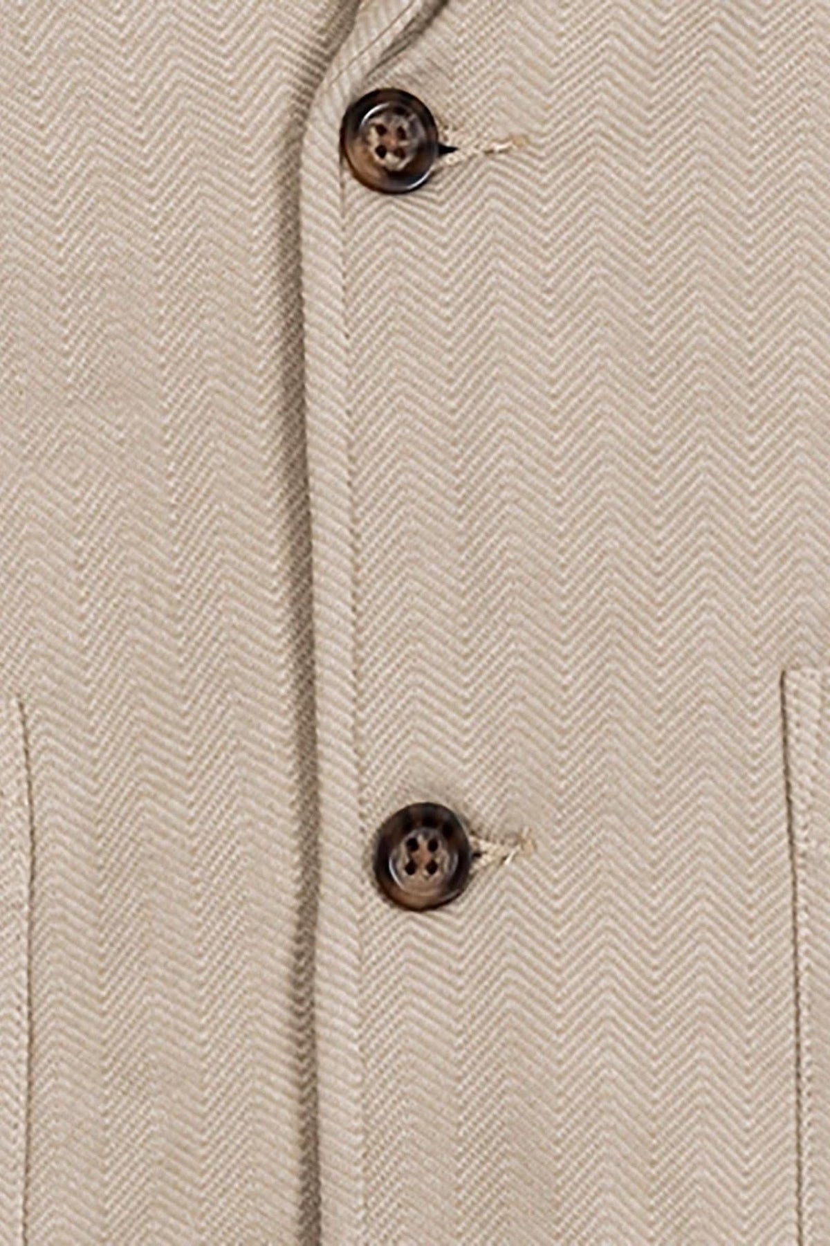 Close-up of a taupe cotton fleece blazer featuring a herringbone pattern, faux horn buttons, and two front patch pockets, highlighting its stylish and comfortable fabric suitable for various occasions.