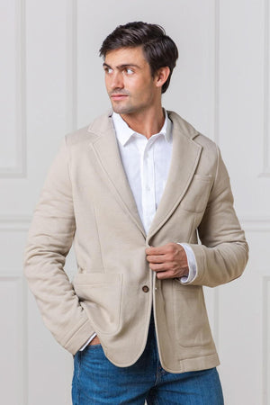 A man wearing a taupe cotton fleece blazer stands against a neutral background. The blazer features a notched lapel and front patch pockets, combining comfort and style effortlessly.