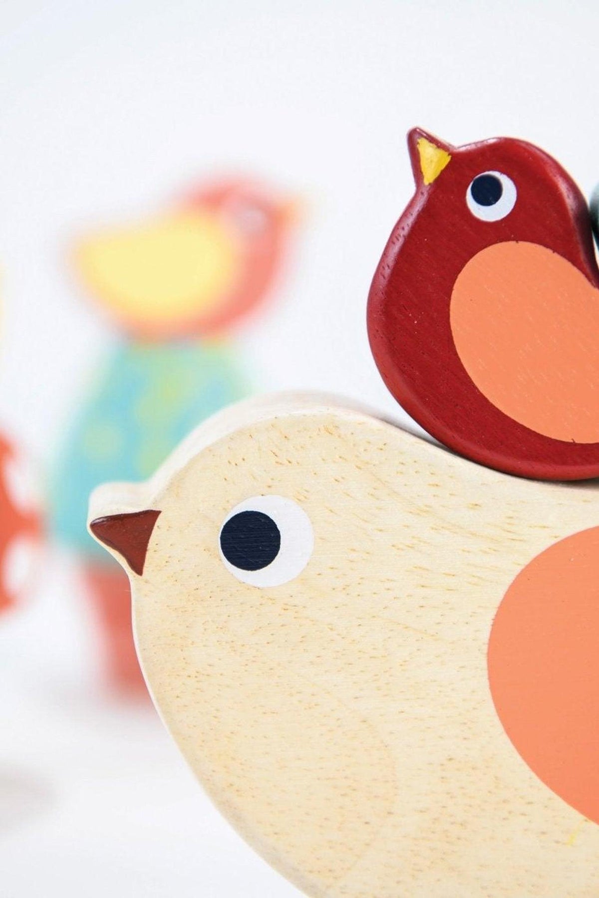 Close-up of colorful wooden bird toys, featuring a beige bird with a red companion, on a light background.