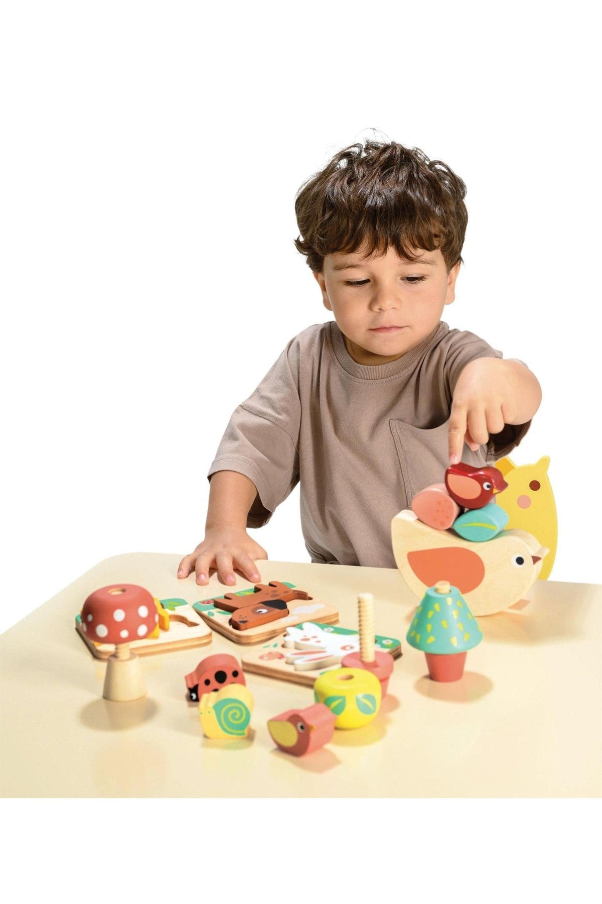 A child plays with colorful wooden toys, including a mushroom and bird, on a beige table.