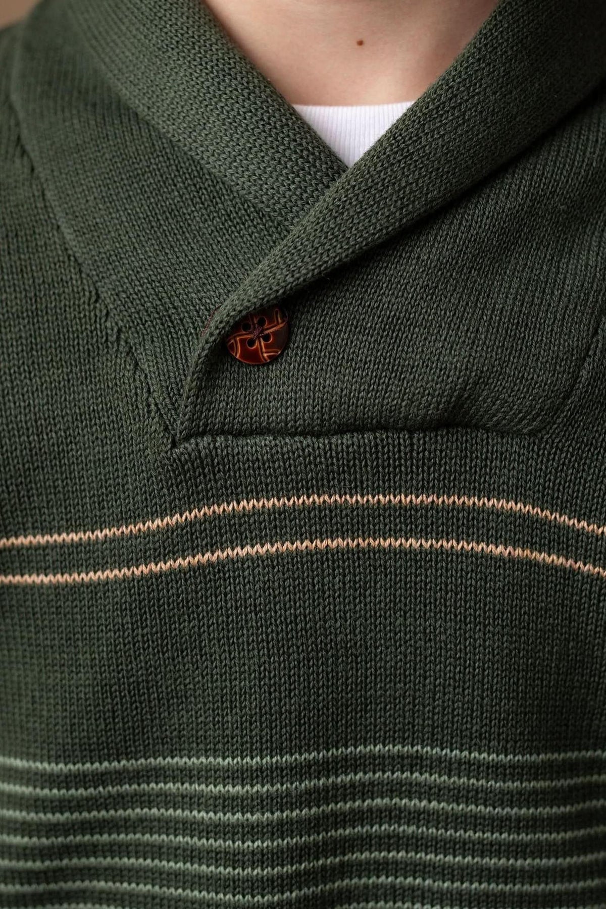 Close-up of a toddler wearing a dark green shawl collar sweater featuring light sage and cream stripes. The sweater is made from soft organic cotton, highlighting its sustainable qualities.