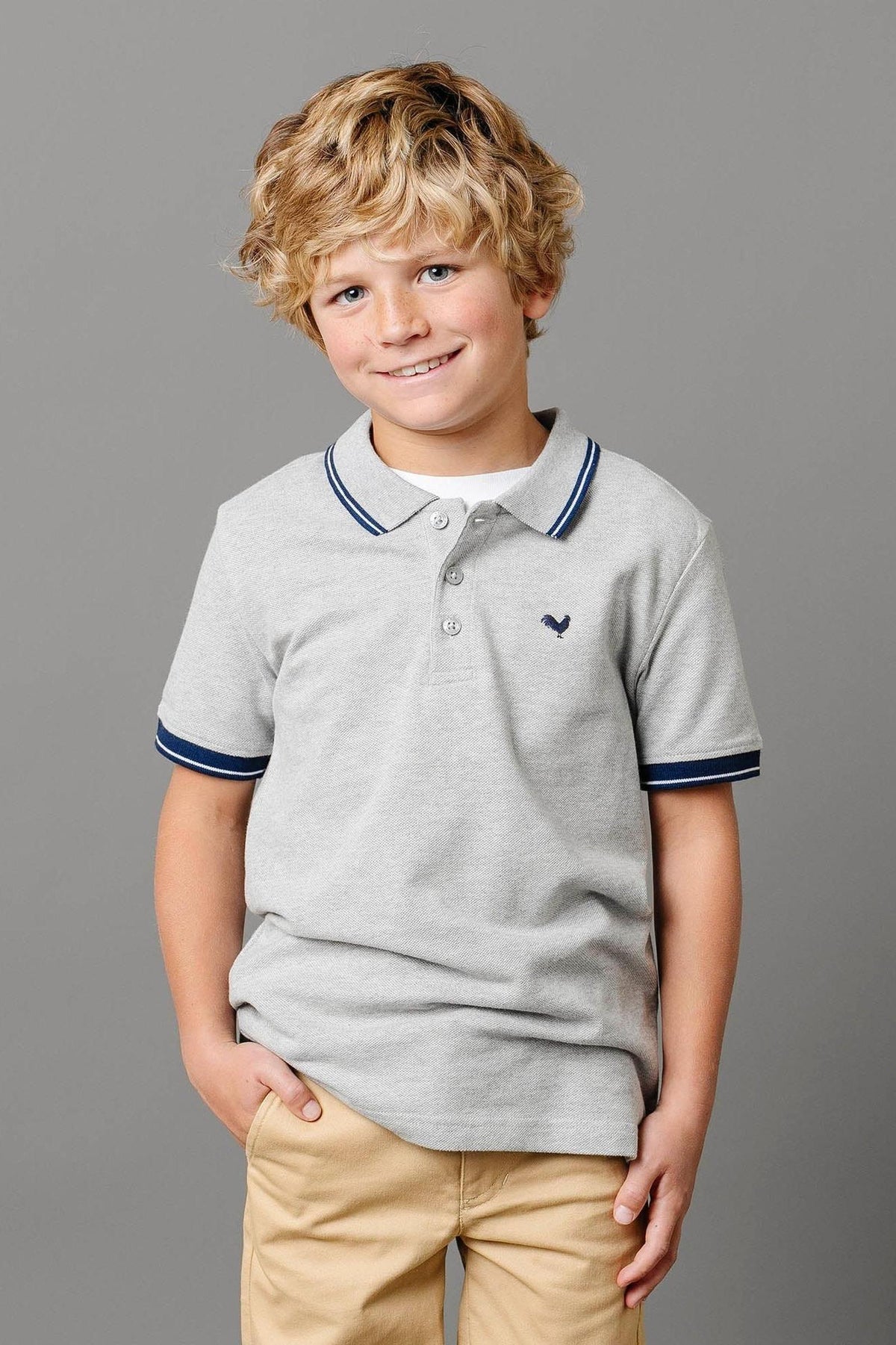 A smiling boy with curly blonde hair wears a light gray polo shirt featuring a flat-knit collar and navy stripes.