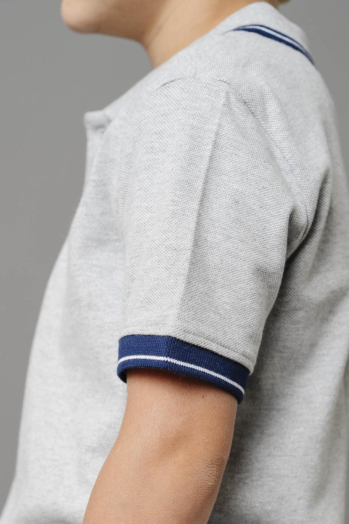 A close-up of a toddler wearing a light gray organic cotton polo shirt with a flat-knit collar and navy blue striped cuffs, showcasing its soft texture and sustainable material.