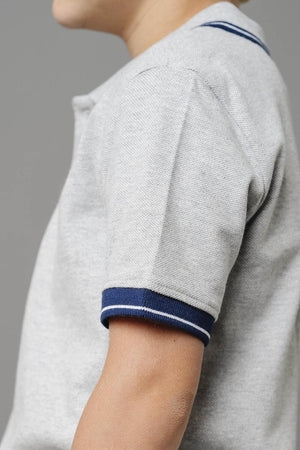 A close-up of a toddler wearing a light gray organic cotton polo shirt with a flat-knit collar and navy blue striped cuffs, showcasing its soft texture and sustainable material.