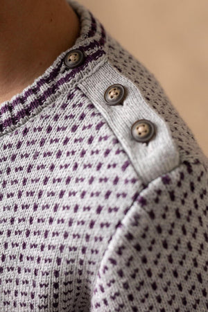 Close-up of a gray and plum intarsia sweater featuring a ribbed collar and three decorative buttons on the shoulder.