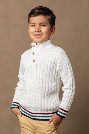 A smiling young boy wears a white cable-knit sweater with a mock neck and faux horn buttons, featuring striped trim at the cuffs and hem, showcasing organic cotton material.