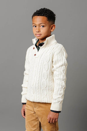 A young boy poses in a white cable knit mock neck sweater with buttons, showcasing a textured design. The sweater is crafted from soft, GOTS-certified organic cotton, perfect for kids.