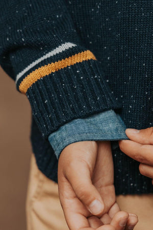 Close-up of a navy organic cotton sweater featuring fleck yarns and athletic tipping, layered over a denim shirt.