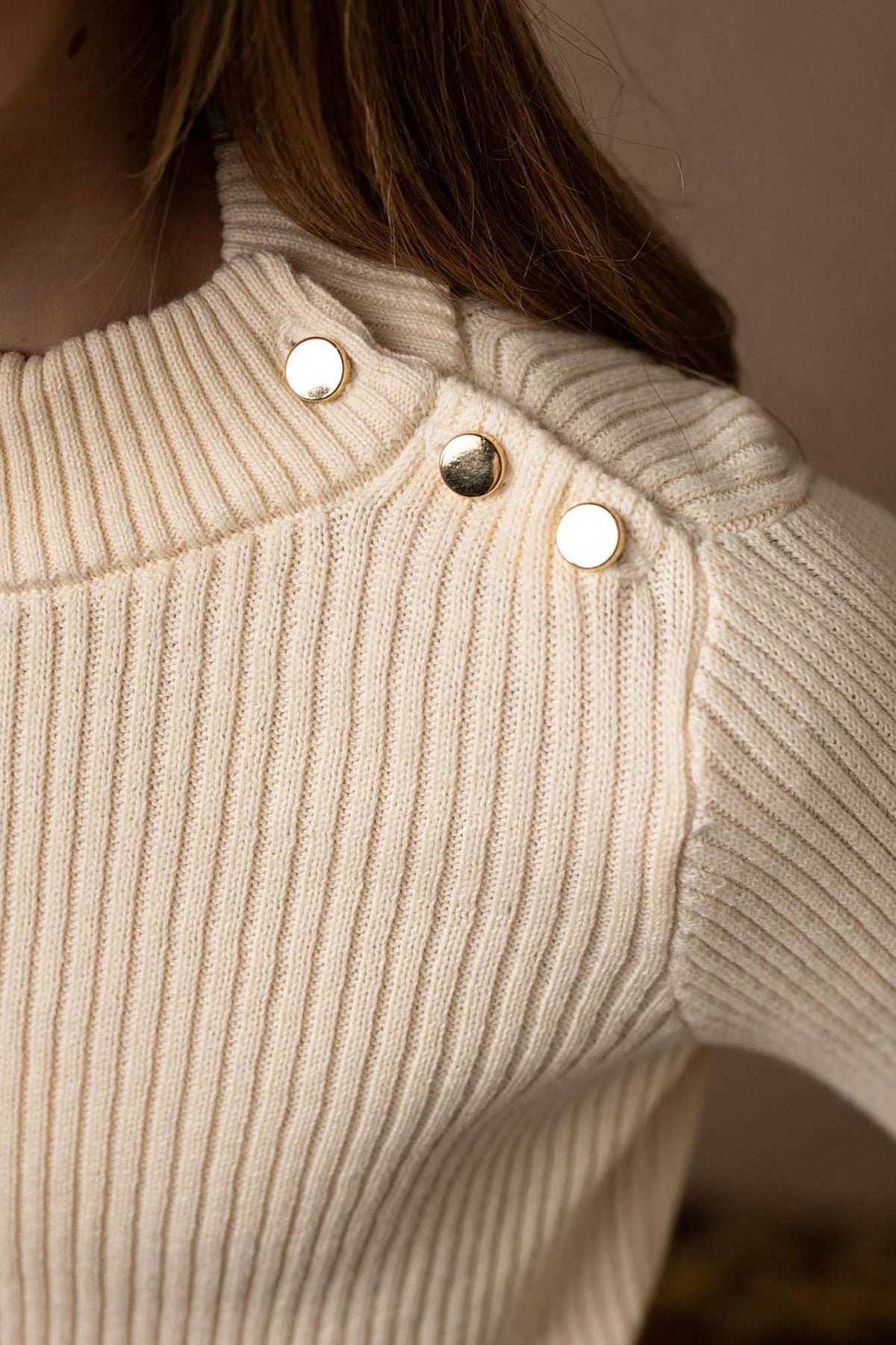Close-up of an ivory mock neck sweater for baby girls, featuring ribbed fabric and three gold button accents on the shoulder, made from soft organic cotton for comfort and style.