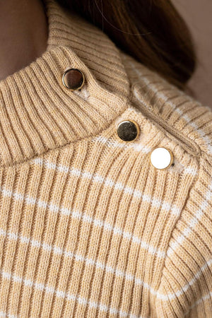 Close-up of a soft, oatmeal-colored sweater featuring a mock neck and gold button details, with delicate white stripes.
