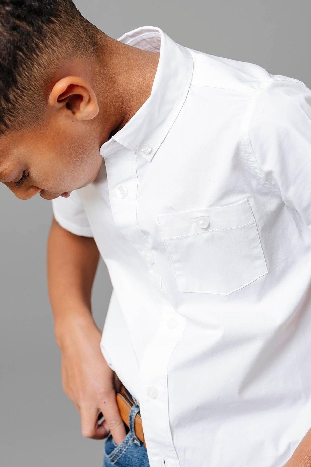 A boy wearing a white short sleeve button-down shirt with a chest pocket, paired with blue jeans.