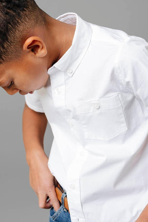 A boy wearing a white short sleeve button-down shirt with a chest pocket, paired with blue jeans.