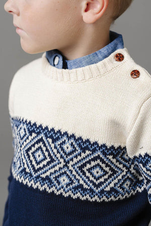 A close-up of a boy wearing a Hope & Henry organic cotton crew neck sweater featuring a cream upper panel and navy lower section with a Fair Isle pattern, complemented.