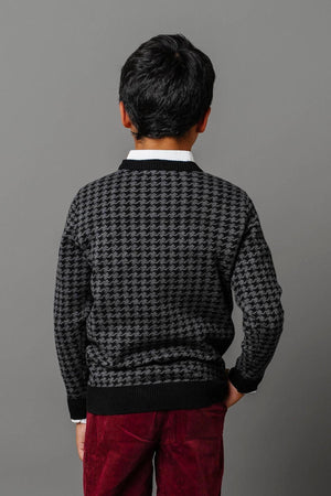 A boy stands with his back facing the camera, wearing a charcoal intarsia knit sweater and burgundy corduroy pants.