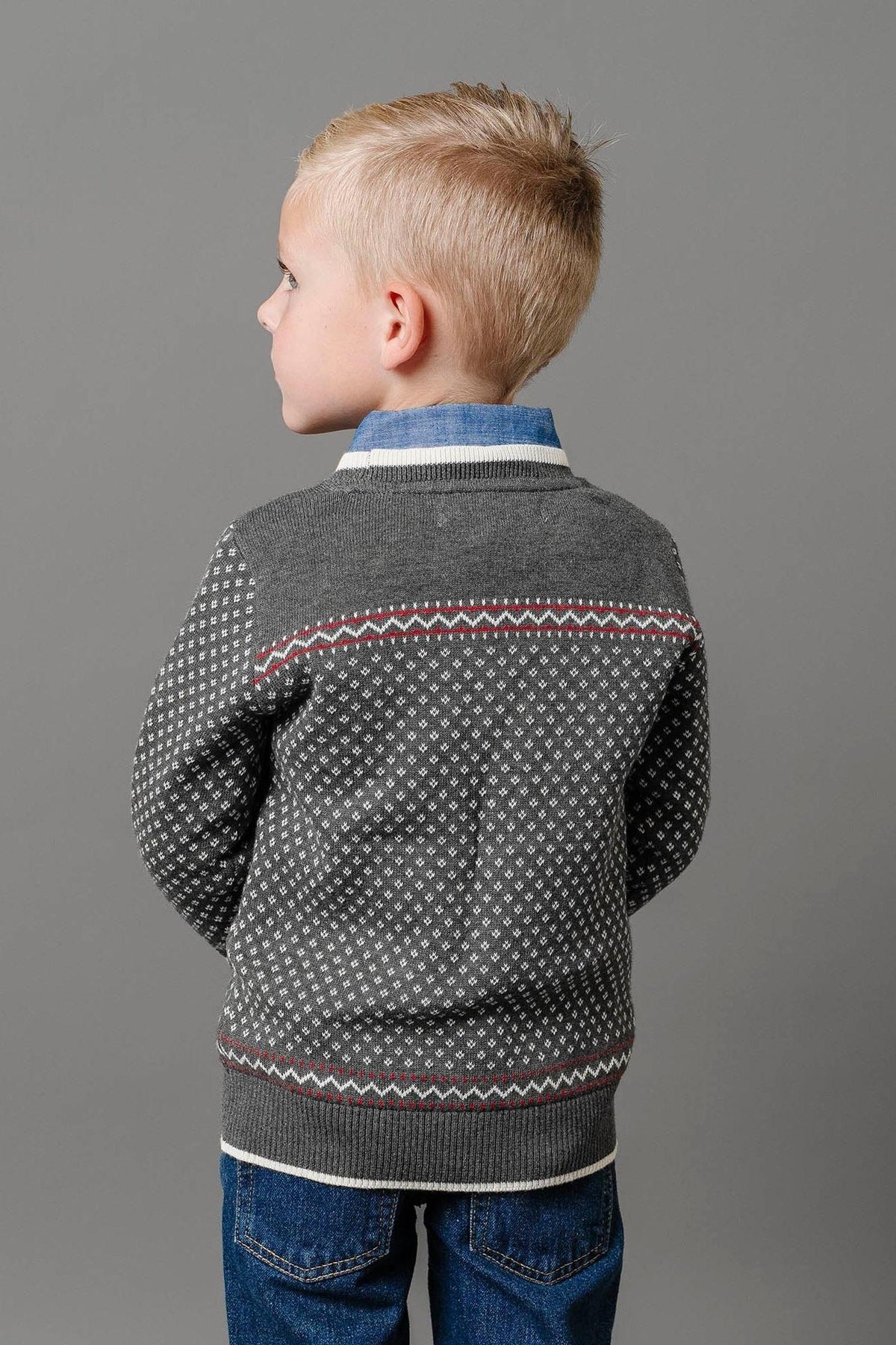 A boy wearing a charcoal heather sweater with an ivory birdseye pattern stands against a gray background.