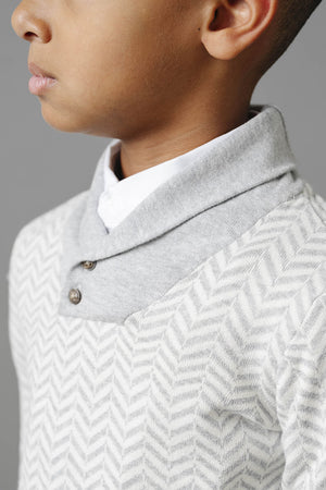 A close-up of a boy wearing a grey herringbone knit shawl collar sweater, showcasing buttons and a white shirt underneath.
