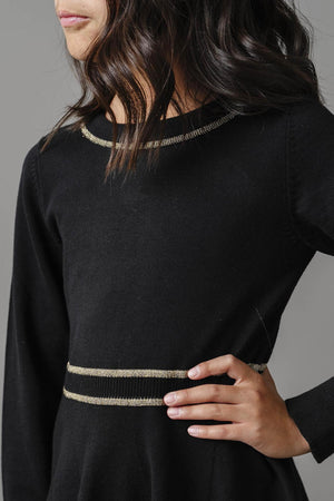 A close-up of a child wearing a black sweater dress with gold-tipped detailing around the neckline and waist.