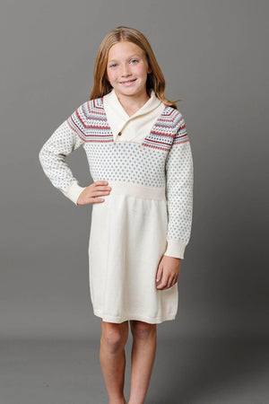 A young girl smiles while wearing an ivory sweater dress with a shawl collar and colorful Nordic patterns.