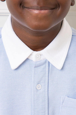 Close-up of a smiling child wearing a light blue pique knit button-down shirt with a white collar.