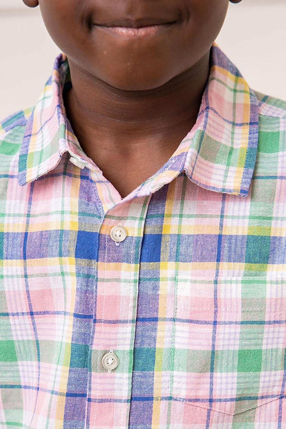 A close-up view of a boy wearing a colorful plaid button-down shirt featuring shades of pink, green, blue, and yellow.