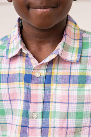 A close-up view of a boy wearing a colorful plaid button-down shirt featuring shades of pink, green, blue, and yellow.