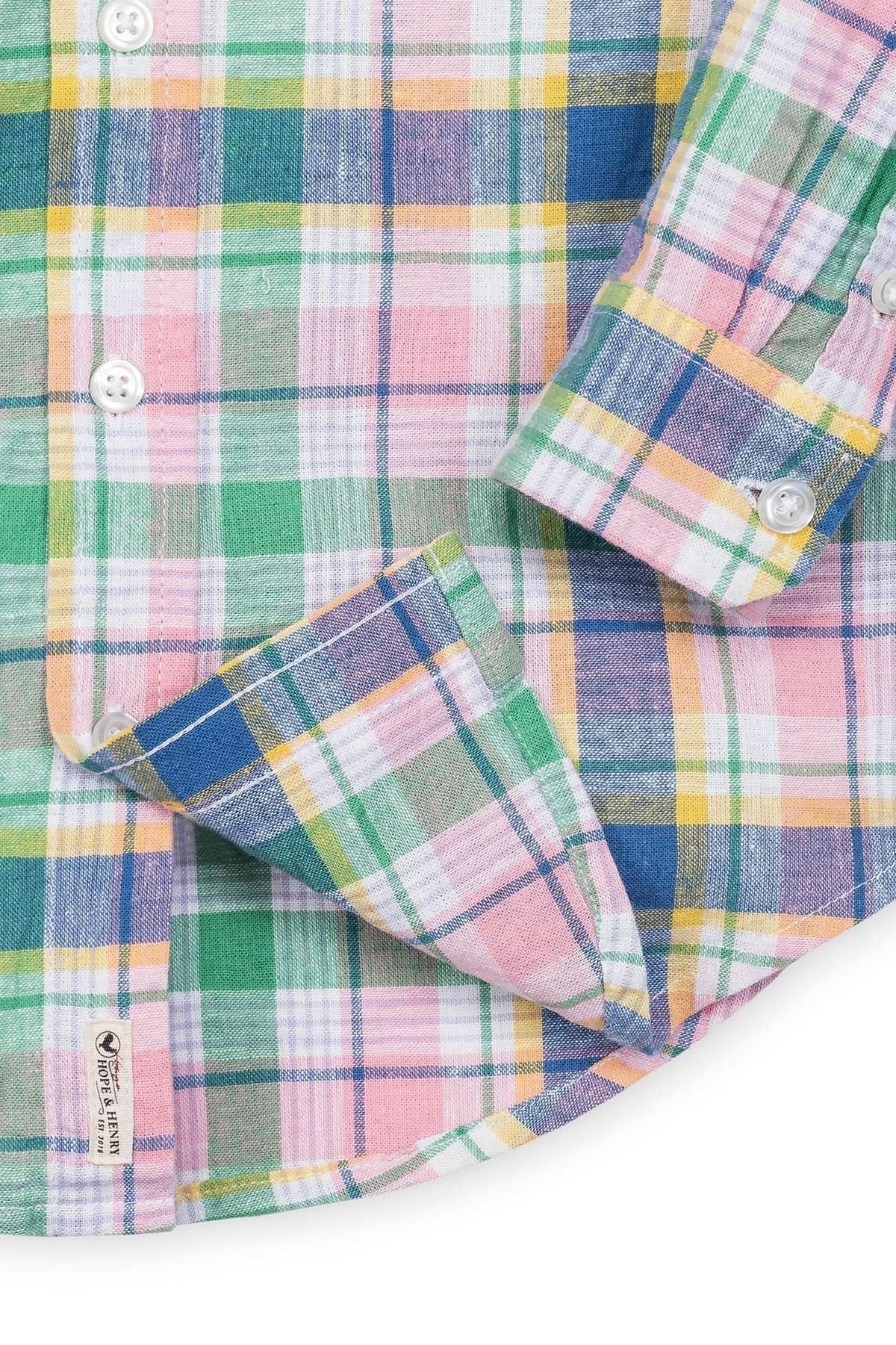 A close-up of a colorful plaid shirt featuring green, pink, blue, and yellow tones, with button details and a label.