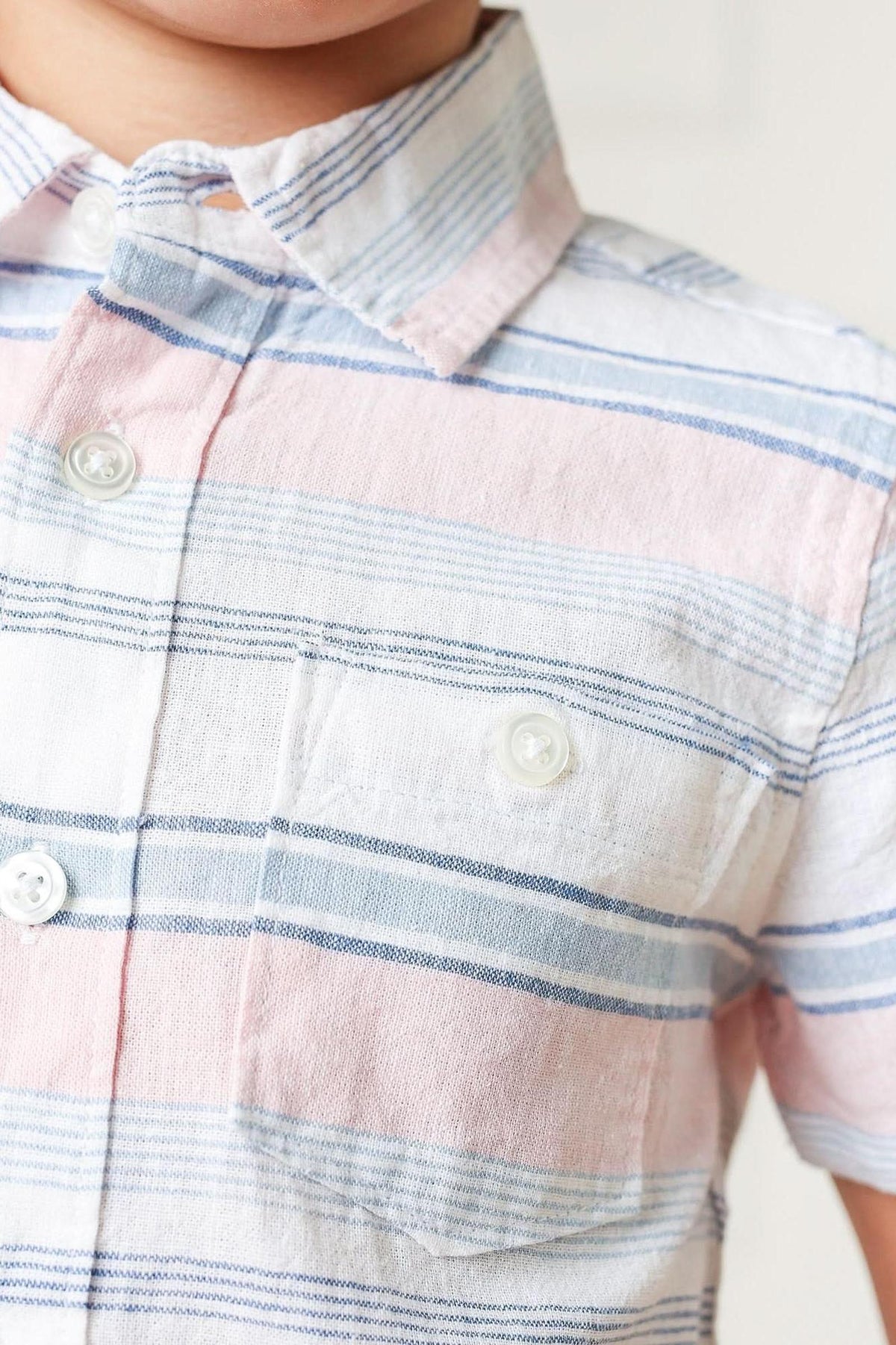Close-up of a short-sleeve button-down shirt for boys featuring a pink and blue striped pattern. The shirt is made from lightweight linen, ideal for warm weather comfort.