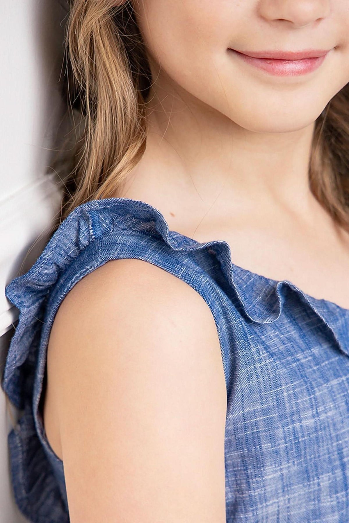 Close-up of a girls shoulder in a blue ruffle neck jumpsuit, showcasing soft organic cotton and delicate ruffle detail.