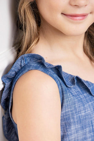 Close-up of a girls shoulder in a blue ruffle neck jumpsuit, showcasing soft organic cotton and delicate ruffle detail.