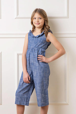 A young girl poses in a chambray organic cotton jumpsuit with a ruffle neck, showcasing a comfortable and stylish design.