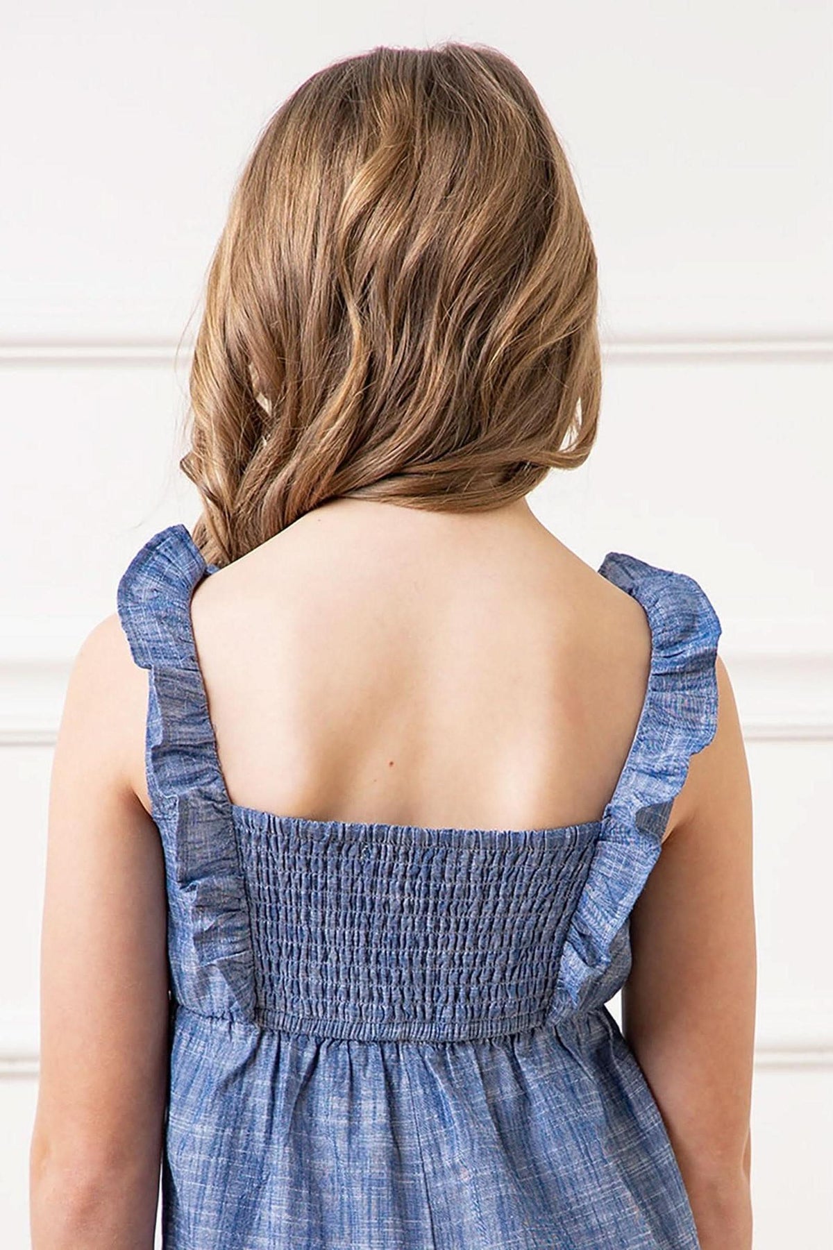 A child wearing a blue organic cotton jumpsuit with ruffled straps and smocked back, showcasing a soft, casual style.