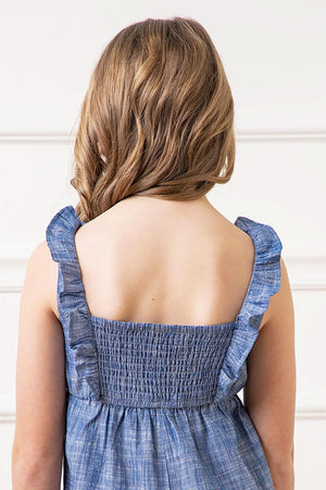 A child wearing a blue organic cotton jumpsuit with ruffled straps and smocked back, showcasing a soft, casual style.