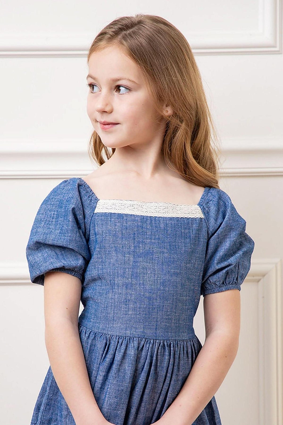 A young girl models a chambray dress with bubble sleeves and a crochet trim, set against a light-colored background.