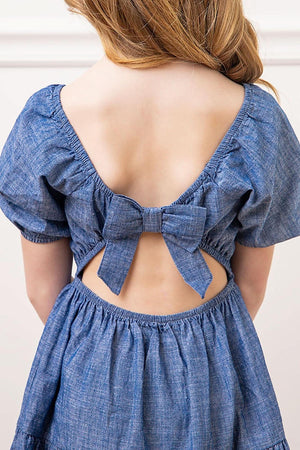 Back view of a chambray dress featuring a bow tie, elastic waistband, and puff sleeves, made from soft organic cotton.