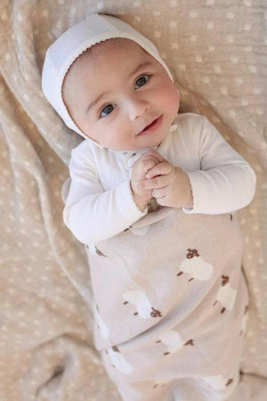 A baby wrapped in a beige swaddle blanket with sheep patterns, lying on a textured background.